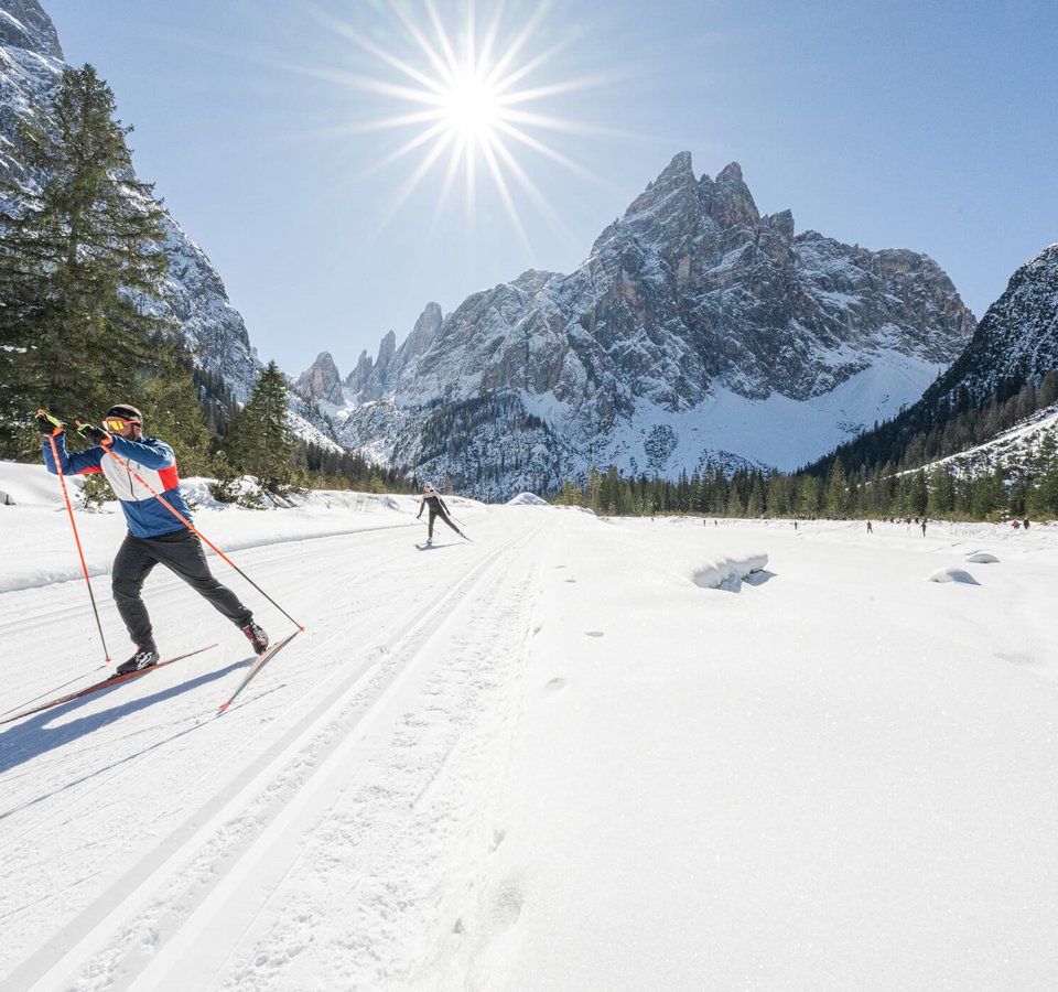 Cross-country skier in snowy mountain valley under bright sun