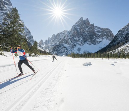 Cross-country skier in snowy mountain valley under bright sun