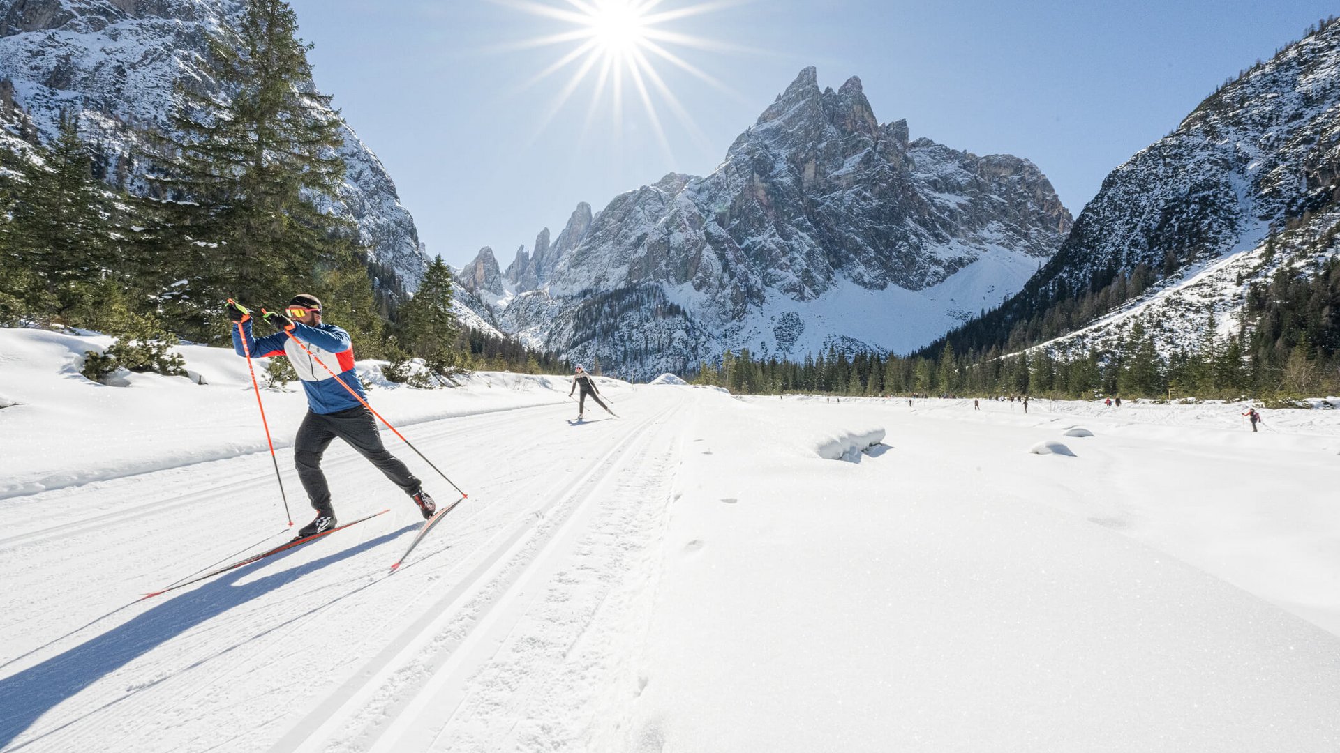 Langläufer im verschneiten Gebirgstal bei strahlendem Sonnenschein