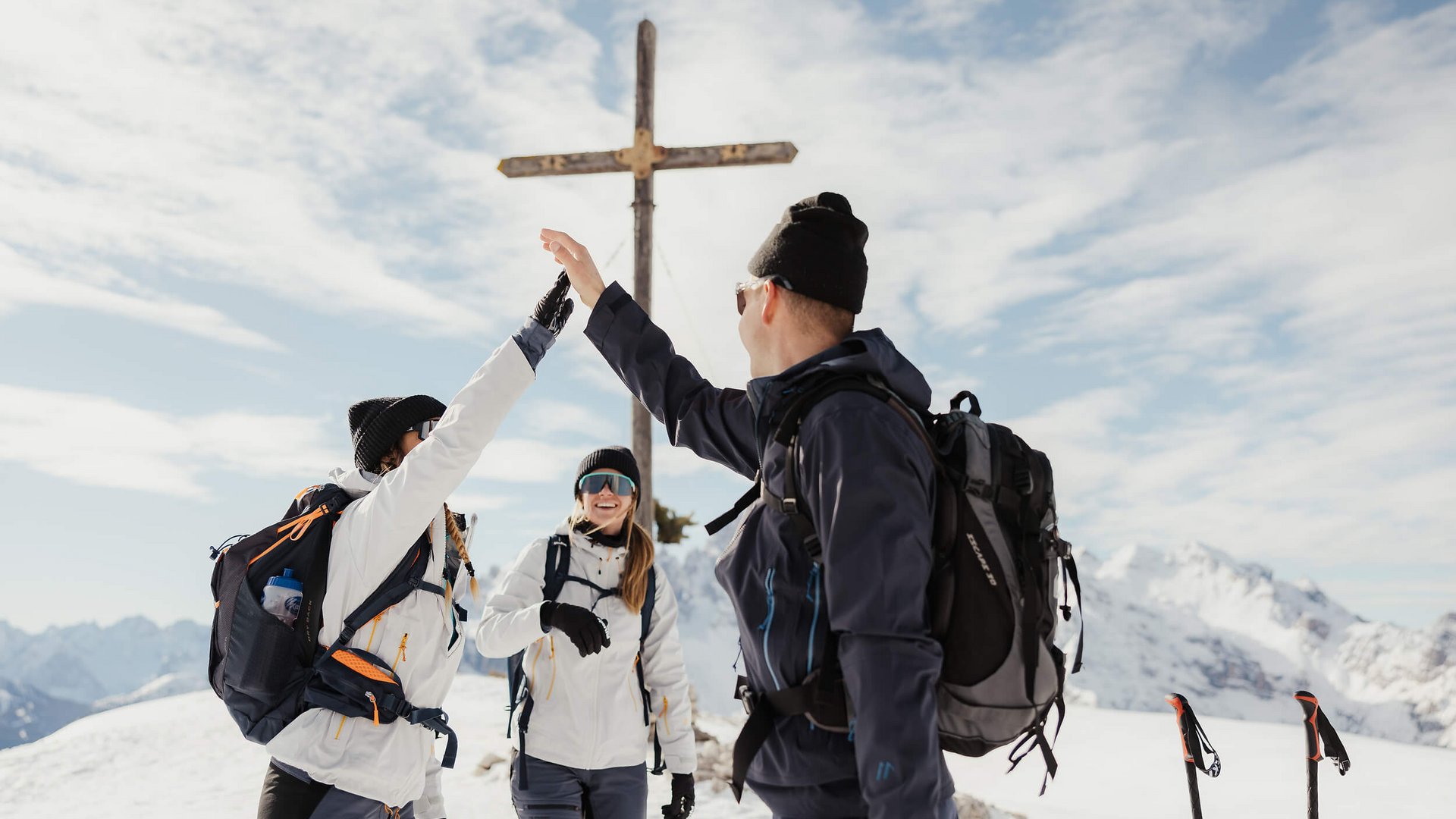 HOW TO SKITOUR © Alex Moling Drei Wanderer geben sich im Schnee an einem Gipfelkreuz einen High Five