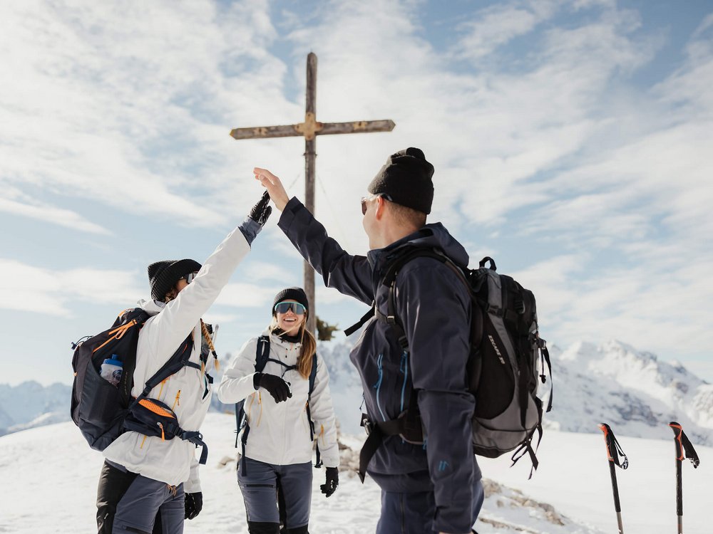 Cross Country Ski Holidays © Alex Moling Three hikers giving a high five near a summit cross in snowy mountains