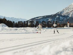 Two cross-country skiers in front of Leutasch sign with snowy mountains in background