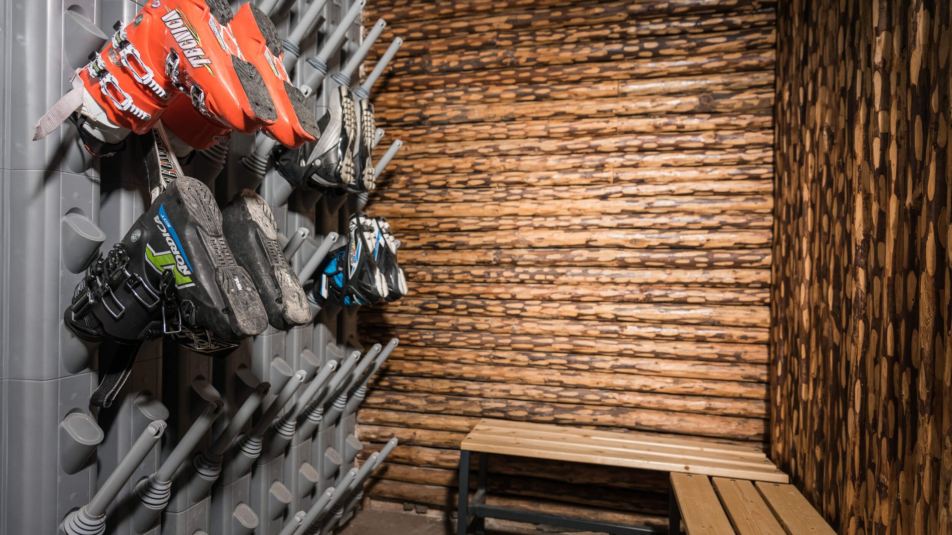Skischuhe hängen zum Trocknen an einer Wand im Skiraum mit Holzwänden