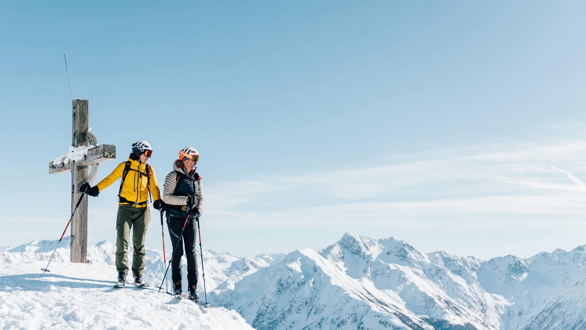 Ski touring holiday in the Passeiertal Valley © Tourismusverein Passeiertal - Benjamin Pfitscher Two skiers standing at a summit cross with snowy mountains in the background