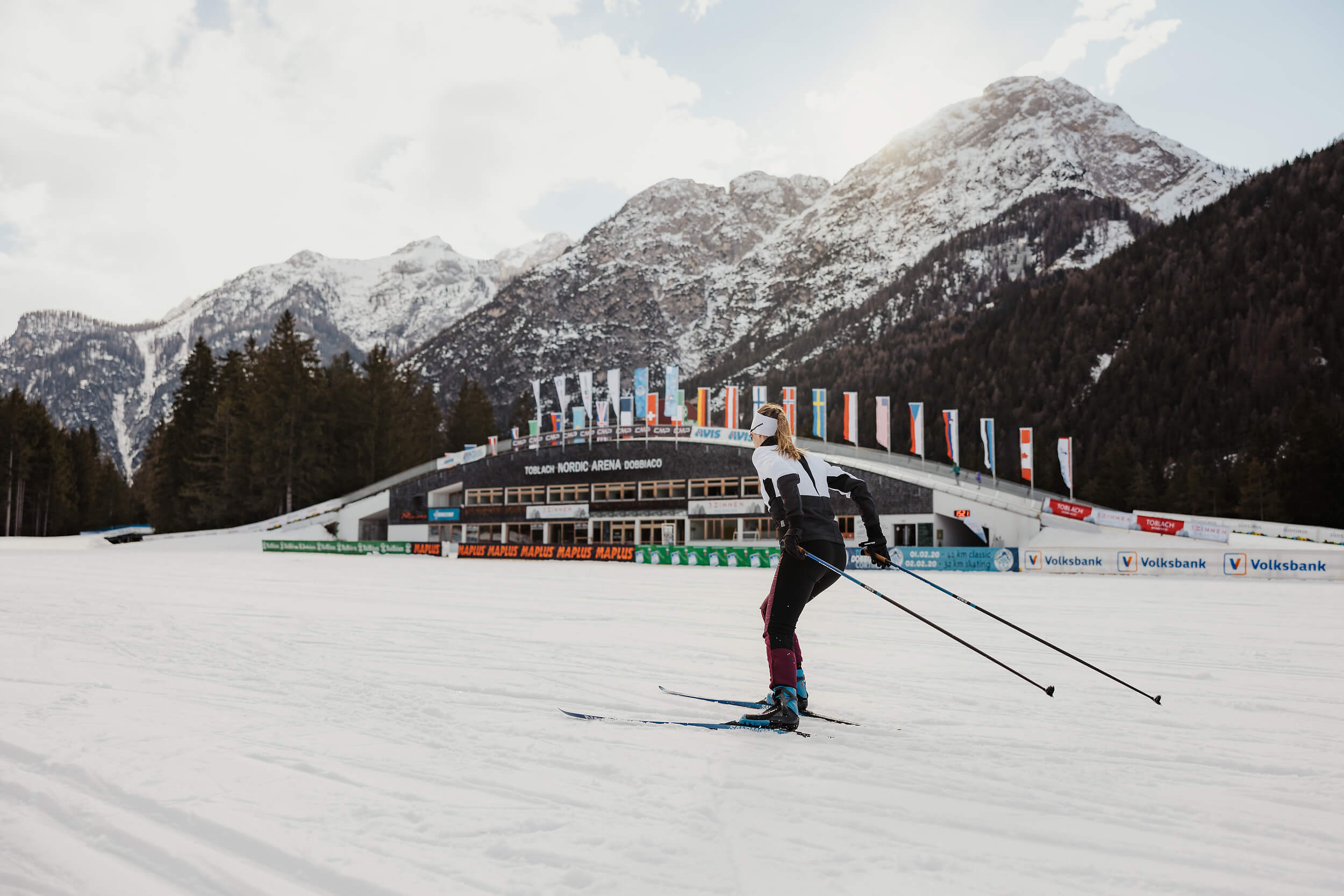 Skilangläufer vor verschneiten Bergen und Nordic Arena in Toblach