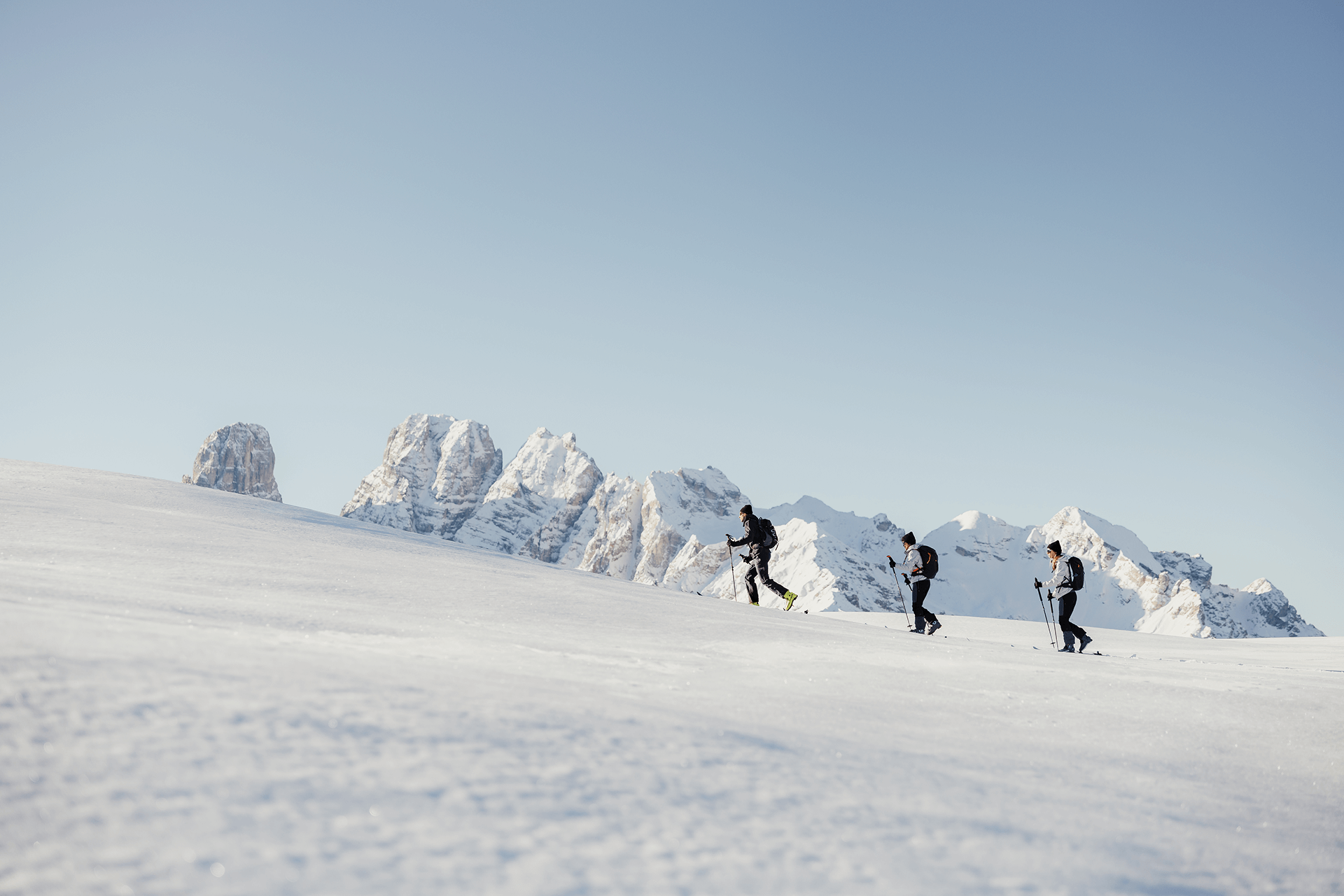 Drei Skitourengeher wandern im Schnee vor schneebedeckten Bergen