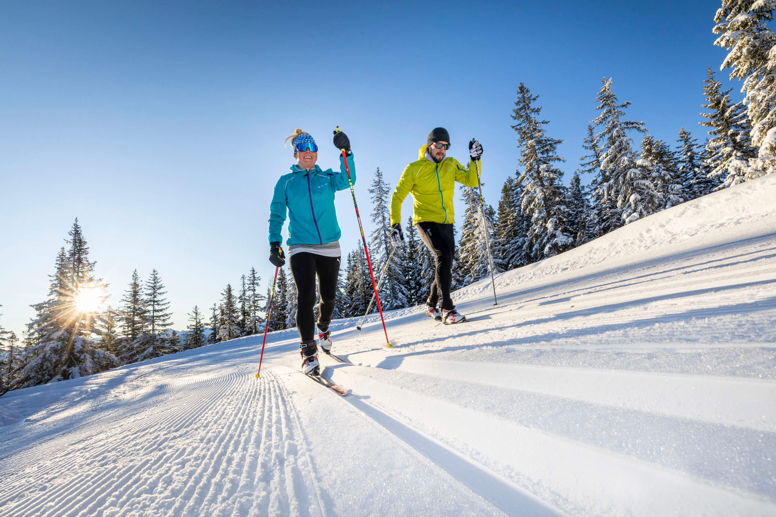 Zwei Personen beim Langlaufen auf verschneiter Loipe im Sonnenschein