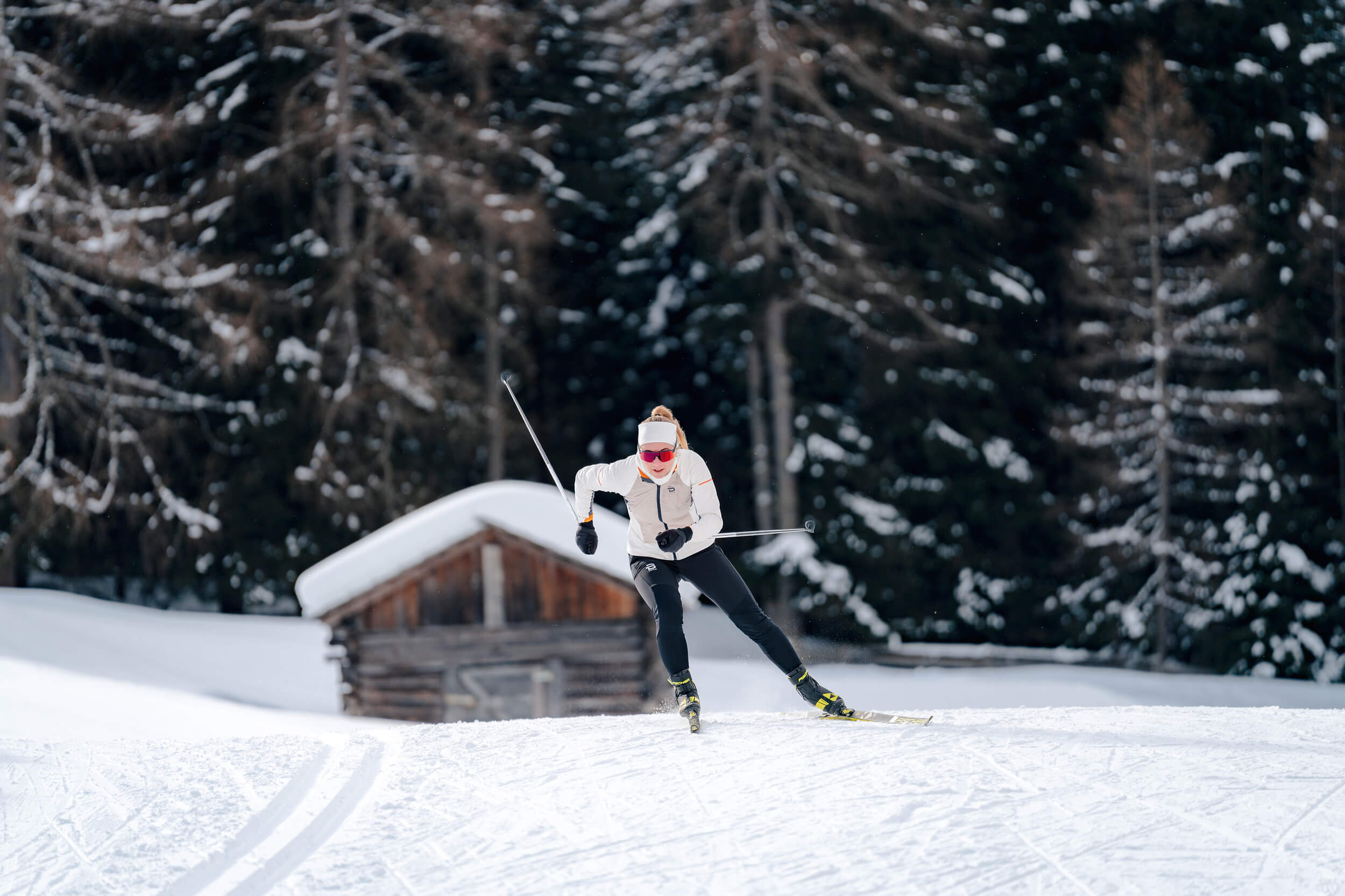 Frau beim Langlaufen vor verschneiter Hütte und Wald