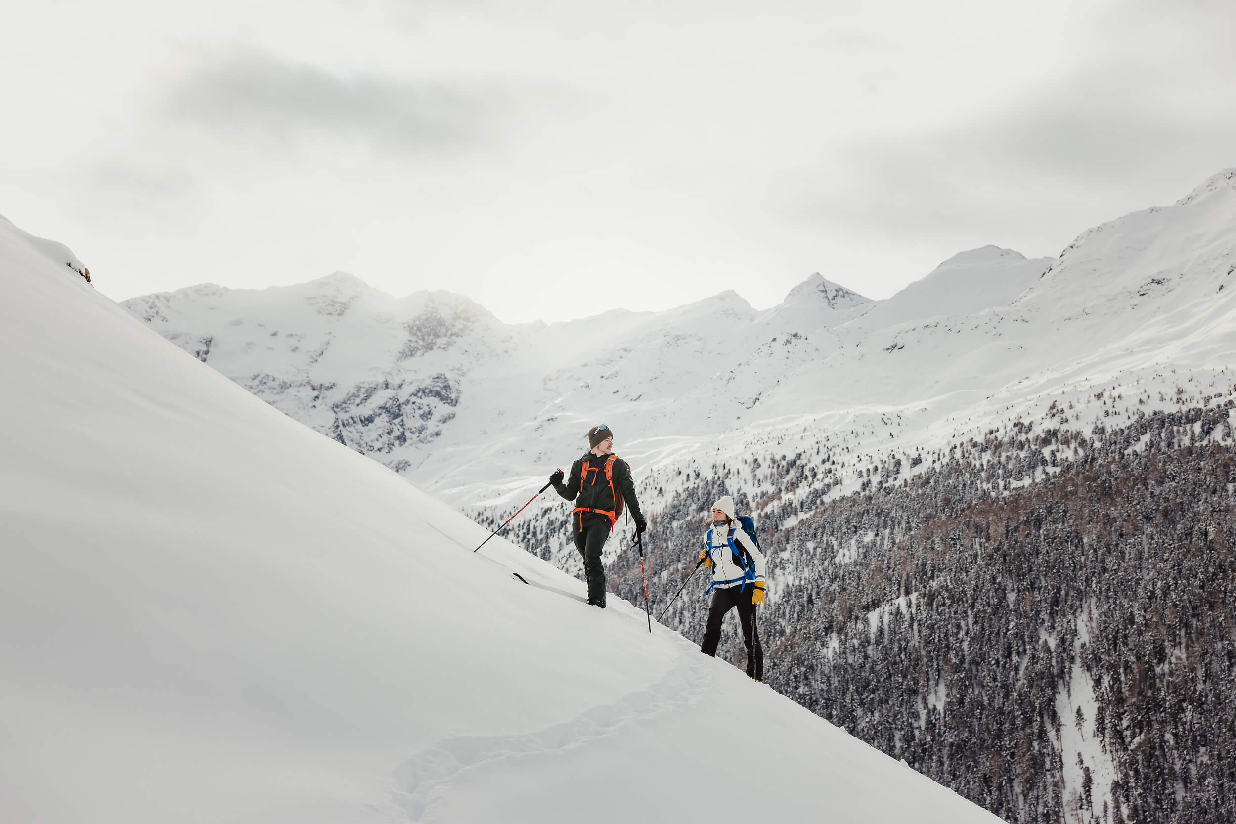 Zwei Wanderer steigen im Schnee an einem steilen Hang in verschneiter Berglandschaft auf
