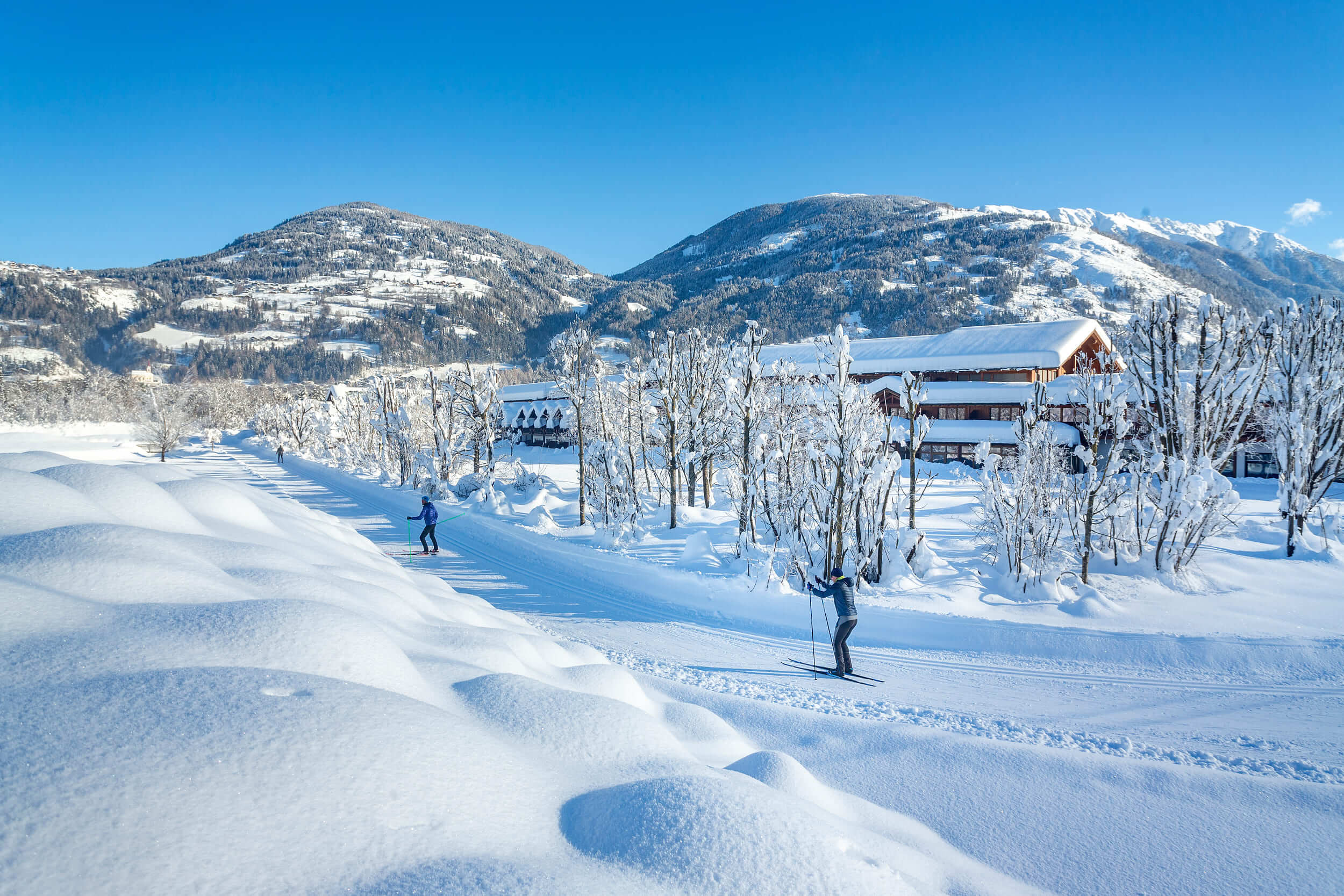 Menschen beim Langlaufen auf schneebedecktem Weg vor Bergkulisse