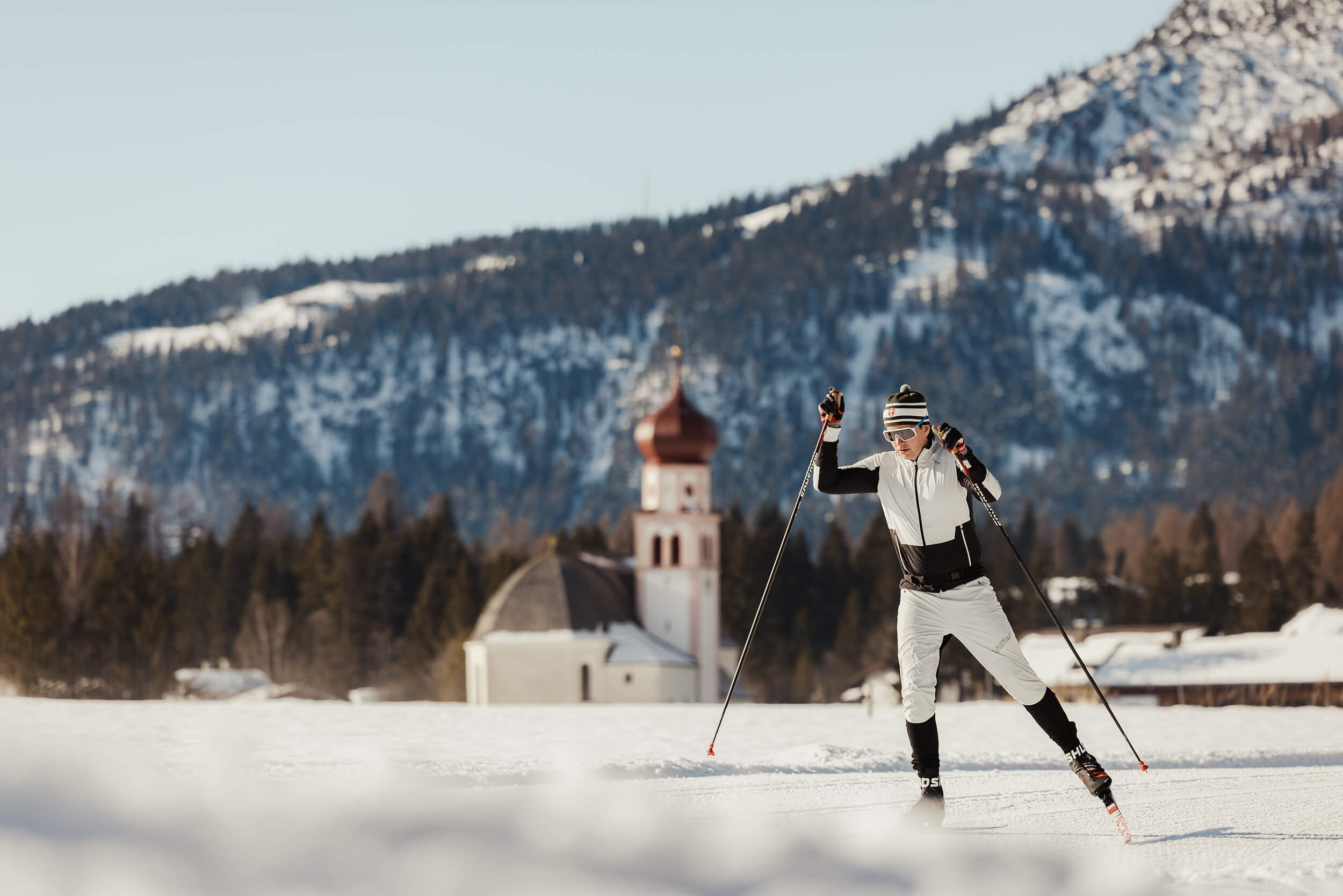 Skilangläufer vor verschneiter Berglandschaft mit Kirche im Hintergrund